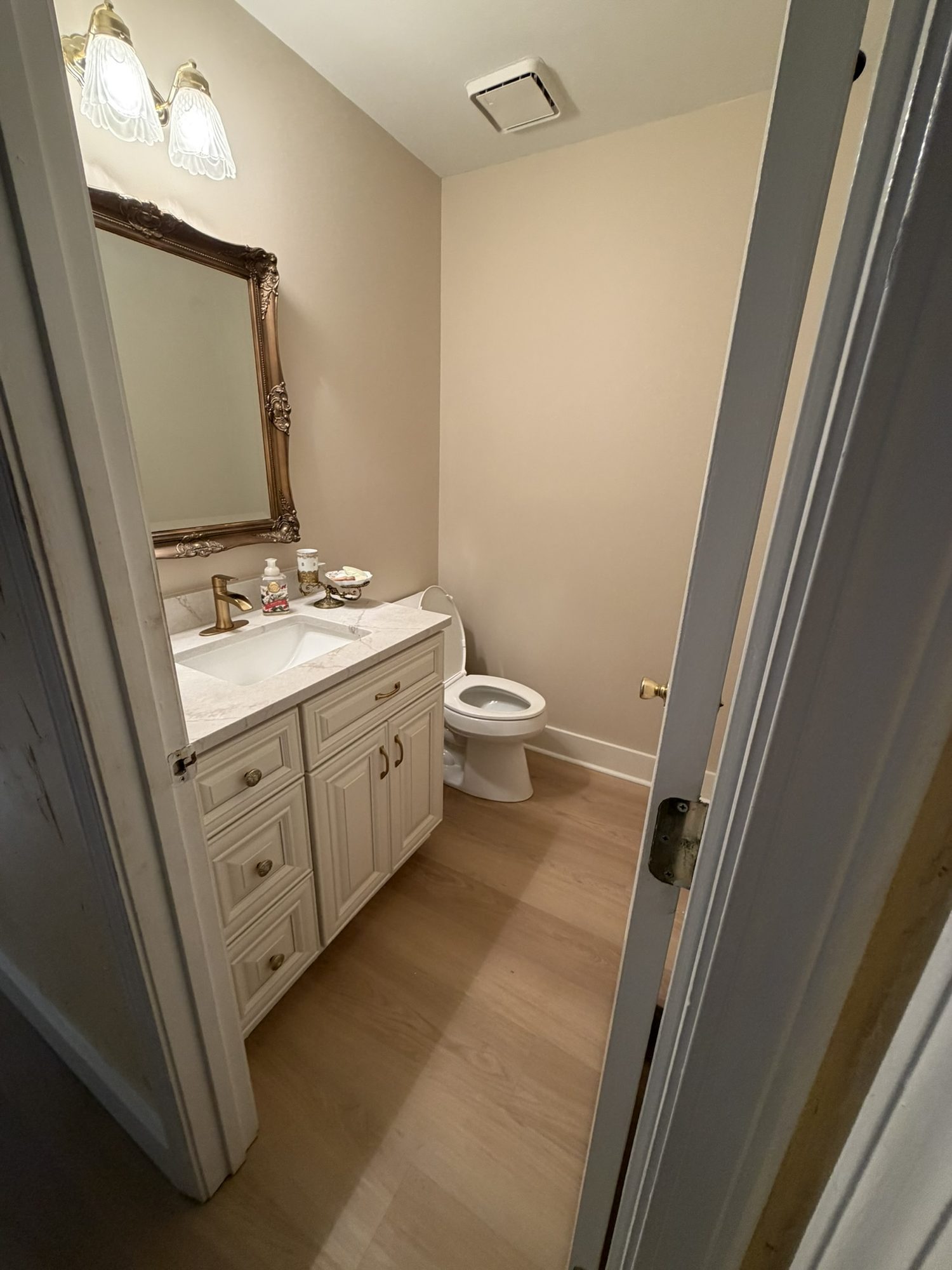 Bathroom with a cream vanity, framed mirror and wood-look floor