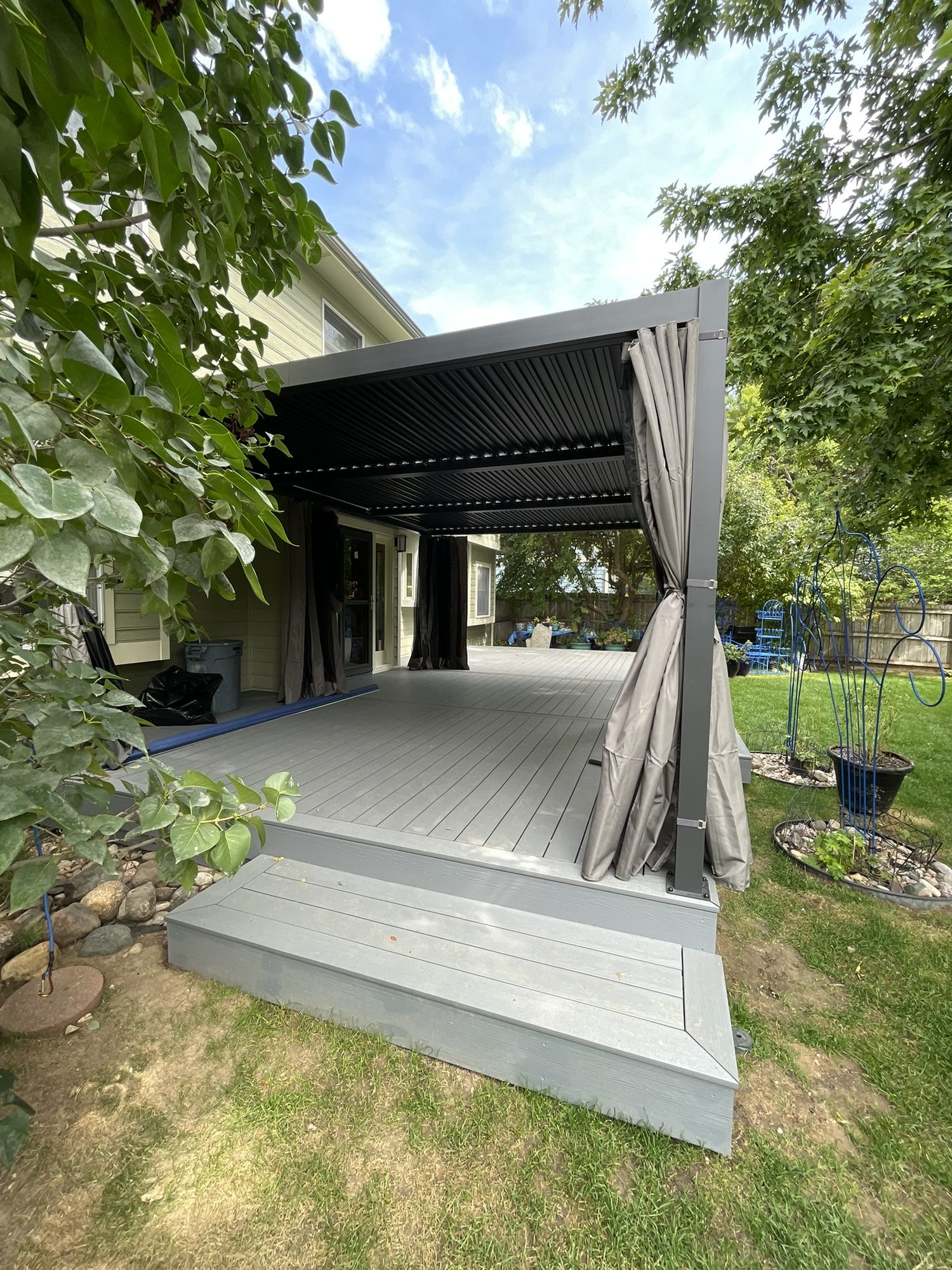 Gray composite deck with a louvered pergola and curtains