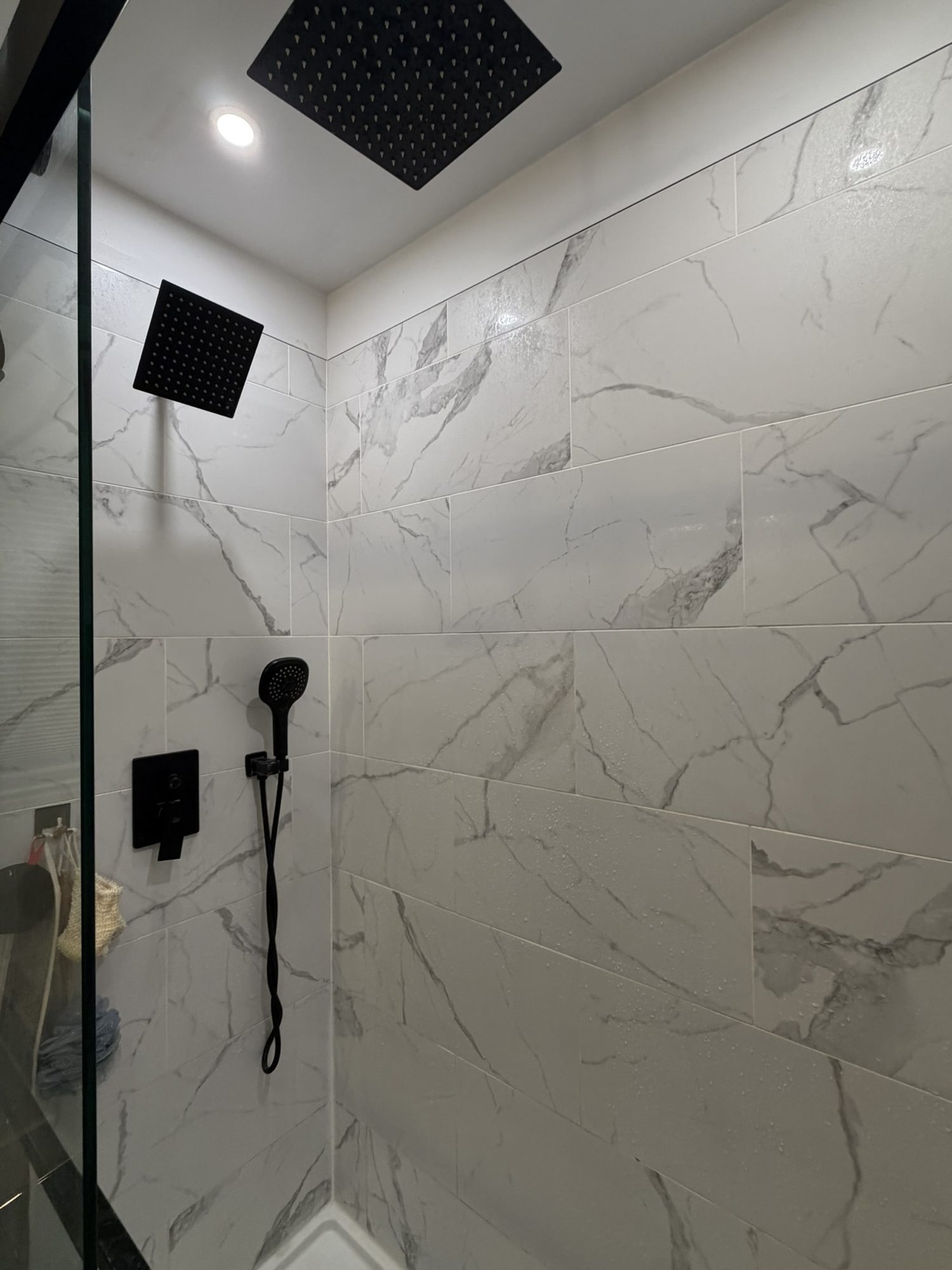 Marble-look tile shower with a ceiling rain head and matte black fixtures