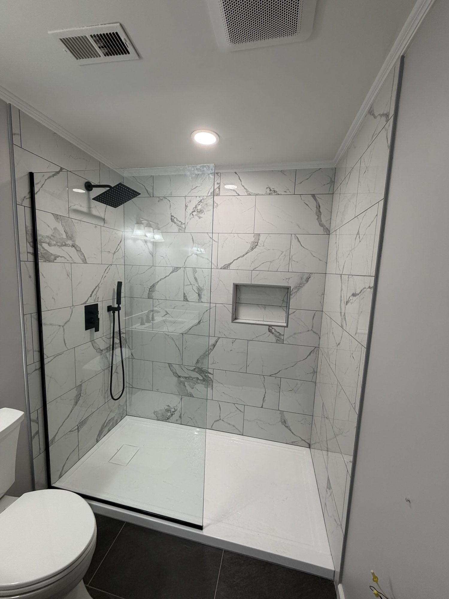 Walk-in tile shower with a recessed niche, glass panel and matte black fixtures