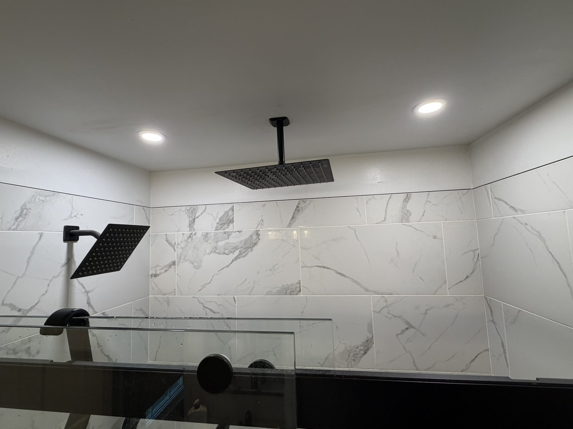 Large marble-look tile shower with a ceiling-mounted rain head